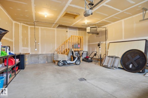 Spacious garage featuring concrete flooring, unpainted drywall walls, overhead lighting, a wooden staircase, and a ceiling-mounted garage door opener - 28 Hewitt Circle, Spruce Grove, AB - Indoor Photo Showing Garage