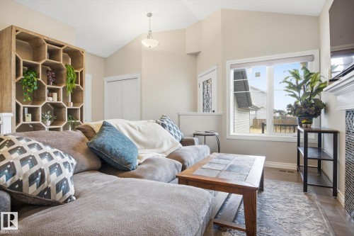 Vaulted ceiling living area featuring a decorative wood-finish shelving unit, a large picture window, and a built-in fireplace - 28 Hewitt Circle, Spruce Grove, AB - Indoor