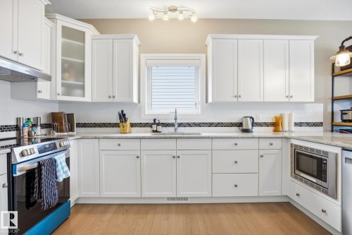 Contemporary kitchen featuring white cabinetry, light-toned wood-finish flooring, a stainless steel range, and a built-in microwave - 28 Hewitt Circle, Spruce Grove, AB - Indoor Photo Showing Kitchen With Double Sink