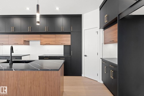 The kitchen features a blend of dark and light wood cabinetry with gold hardware, a black kitchen island with a white veined countertop, and a black sink with a matte black faucet - 94 Blackbird Bend, Fort Saskatchewan, AB - Indoor Photo Showing Kitchen With Double Sink