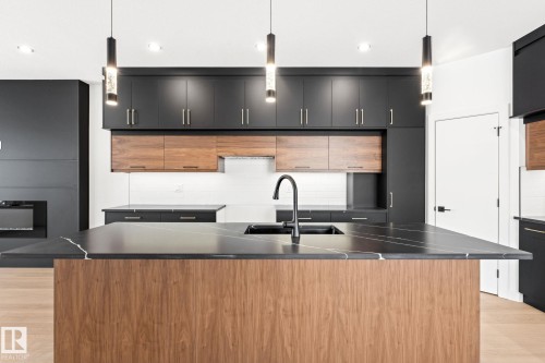 This kitchen features an expansive island with a dark countertop and a wood-paneled base, complemented by dark cabinetry with wood accents - 94 Blackbird Bend, Fort Saskatchewan, AB - Indoor Photo Showing Kitchen With Double Sink With Upgraded Kitchen