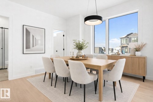 Well-lit dining area featuring light-toned hardwood floors, large windows providing abundant natural light, and a modern overhead light fixture - 94 Blackbird Bend, Fort Saskatchewan, AB - Indoor Photo Showing Dining Room
