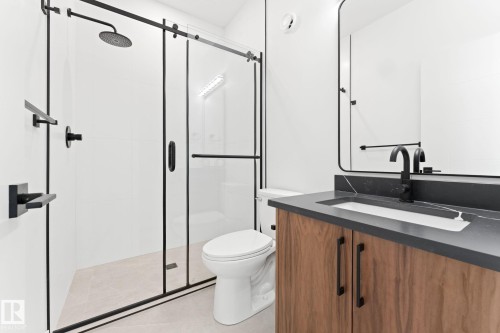 Bathroom featuring a glass-enclosed shower with matte black fixtures, a contemporary vanity with a dark countertop and integrated sink, and a framed mirror - 94 Blackbird Bend, Fort Saskatchewan, AB - Indoor Photo Showing Bathroom