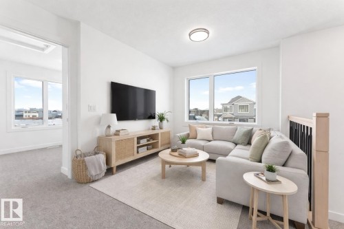 Bright living area featuring a large window with views of surrounding properties, light-colored carpeting, and a contemporary ceiling light fixture - 94 Blackbird Bend, Fort Saskatchewan, AB - Indoor Photo Showing Living Room