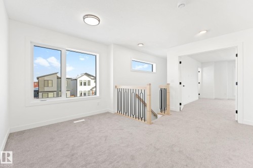 This bright interior space features light-colored carpeting, a large window providing natural light, and a staircase with a wooden handrail and black metal spindles - 94 Blackbird Bend, Fort Saskatchewan, AB - Indoor Photo Showing Other Room