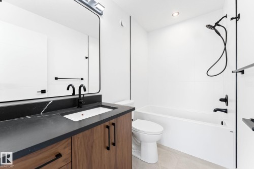 Bathroom featuring a modern vanity with a dark countertop and an undermount sink, a sleek black-framed mirror, and a full-sized bathtub with a shower - 94 Blackbird Bend, Fort Saskatchewan, AB - Indoor Photo Showing Bathroom