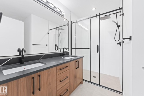 Bathroom featuring a double vanity with two sinks, dark countertops, and wood cabinetry - 94 Blackbird Bend, Fort Saskatchewan, AB - Indoor Photo Showing Bathroom