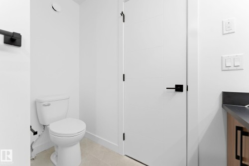 This bathroom features a white toilet, light-colored floor tiling, and a white interior door with black hardware - 94 Blackbird Bend, Fort Saskatchewan, AB - Indoor Photo Showing Bathroom