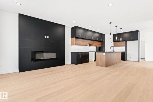 This open-concept area features light-toned flooring, a sleek black accent wall with an integrated fireplace, and recessed lighting - 94 Blackbird Bend, Fort Saskatchewan, AB - Indoor Photo Showing Kitchen