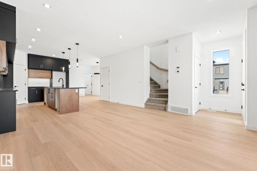The property features light-toned hardwood flooring, a modern kitchen with dark cabinetry and a central island, and a staircase with carpeted treads - 94 Blackbird Bend, Fort Saskatchewan, AB - Indoor Photo Showing Kitchen With Upgraded Kitchen