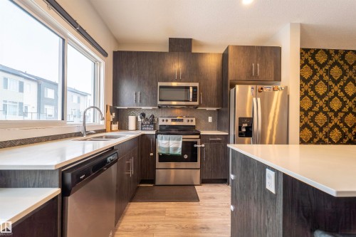 Contemporary kitchen featuring dark wood-finish cabinetry, stainless steel appliances, and light countertops - 117 804 Welsh Drive, Edmonton, AB - Indoor Photo Showing Kitchen With Double Sink With Upgraded Kitchen