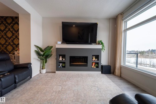 Living area with a built-in electric fireplace, integrated shelving, and large windows - 117 804 Welsh Drive, Edmonton, AB - Indoor Photo Showing Living Room With Fireplace