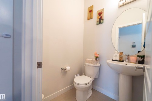 Powder room featuring a pedestal sink, round mirror, and tile flooring - 117 804 Welsh Drive, Edmonton, AB - Indoor Photo Showing Bathroom