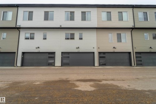 Modern townhome exterior featuring multi-toned horizontal siding, dark-framed windows, and contemporary garage doors with frosted glass inserts - 117 804 Welsh Drive, Edmonton, AB - Outdoor