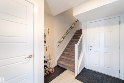 Entryway featuring a paneled door, carpeted staircase with glass railing, and tiled flooring - 117 804 Welsh Drive, Edmonton, AB - Indoor Photo Showing Other Room