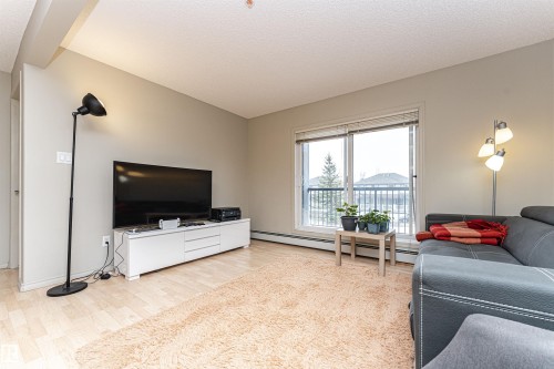 Living area featuring light-toned flooring, neutral wall paint, and a large window with a balcony - 219 646 Mcallister Loop, Edmonton, AB - Indoor Photo Showing Living Room