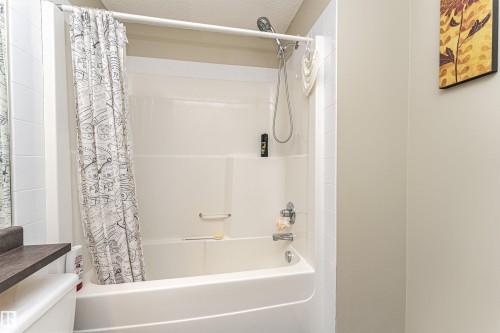 White fiberglass tub and shower combination with a curved shower curtain rod, a chrome shower head, and a built-in soap shelf - 219 646 Mcallister Loop, Edmonton, AB - Indoor Photo Showing Bathroom