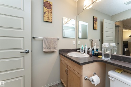 Bathroom featuring a light-toned vanity with a built-in sink, dark countertop, and large wall-mounted mirror - 219 646 Mcallister Loop, Edmonton, AB - Indoor Photo Showing Bathroom