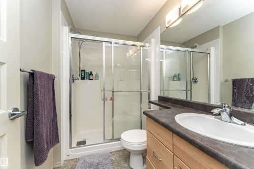 Bathroom featuring a glass-enclosed shower, a vanity with wood-finish cabinetry, a white drop-in sink, and a dark countertop - 219 646 Mcallister Loop, Edmonton, AB - Indoor Photo Showing Bathroom
