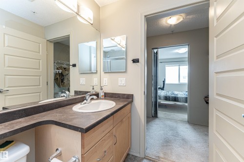 Bathroom vanity featuring a single basin sink, dark countertop, and light wood-finish cabinetry - 219 646 Mcallister Loop, Edmonton, AB - Indoor Photo Showing Bathroom