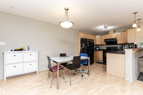 Kitchen area featuring light wood-finish flooring, light wood cabinetry, black appliances, and a breakfast bar with pendant lighting - 219 646 Mcallister Loop, Edmonton, AB - Indoor Photo Showing Other Room