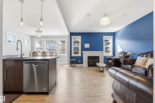 Open-concept living area featuring wood-finish flooring, a contemporary fireplace with a tiled surround, a kitchen island with built-in dishwasher, and ample natural light from multiple windows - 9812 224 Street, Edmonton, AB - Indoor With Fireplace