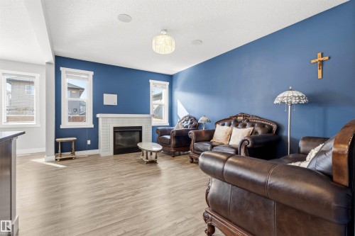 Living area featuring wood-finish flooring, multiple windows, a ceiling-mounted light fixture, and a fireplace with a white tile surround and mantel - 9812 224 Street, Edmonton, AB - Indoor Photo Showing Living Room With Fireplace