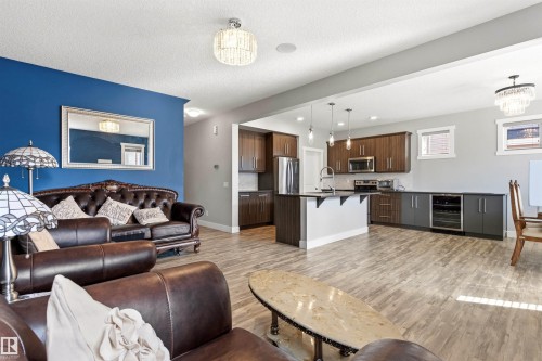 Open-concept living space featuring wood-finish flooring throughout, a kitchen island with pendant lighting, stainless steel appliances, and a built-in beverage cooler - 9812 224 Street, Edmonton, AB - Indoor