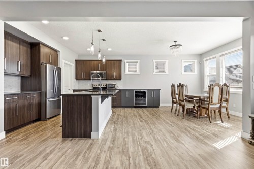 Open-concept kitchen and dining area featuring wood-finish flooring, dark wood cabinetry, a central island with a breakfast bar, stainless steel appliances, and a built-in beverage cooler - 9812 224 Street, Edmonton, AB - Indoor Photo Showing Kitchen With Stainless Steel Kitchen With Upgraded Kitchen