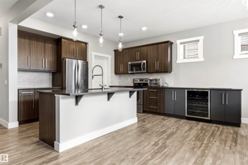 Modern kitchen featuring dark wood-finish cabinetry, stainless steel appliances, a center island with pendant lighting, and wood-finish flooring - 9812 224 Street, Edmonton, AB - Indoor Photo Showing Kitchen With Stainless Steel Kitchen With Upgraded Kitchen