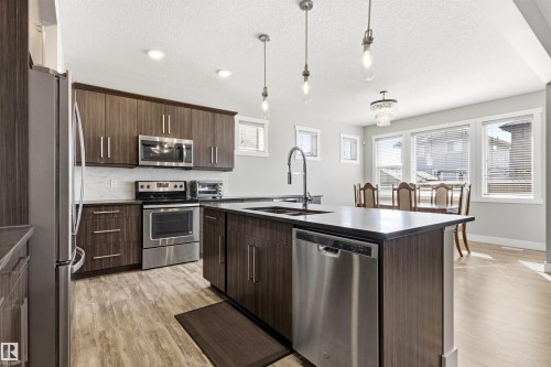 Contemporary kitchen featuring dark wood-finish cabinetry, stainless steel appliances, a center island with sink, and light wood-finish flooring - 9812 224 Street, Edmonton, AB - Indoor Photo Showing Kitchen With Stainless Steel Kitchen With Double Sink With Upgraded Kitchen