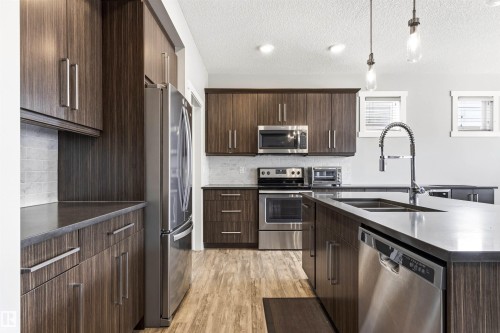 Kitchen featuring dark wood-finish cabinetry, stainless steel appliances, a tile backsplash, and an island with an undermount sink and gooseneck faucet - 9812 224 Street, Edmonton, AB - Indoor Photo Showing Kitchen With Stainless Steel Kitchen With Double Sink With Upgraded Kitchen
