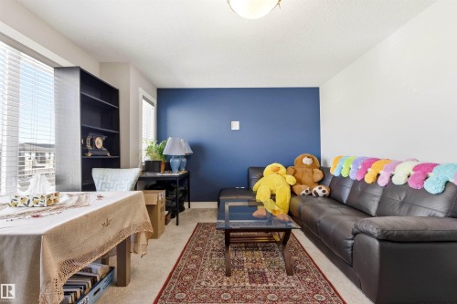 Light-filled room featuring a deep blue accent wall, neutral carpeting, and a built-in shelving unit - 9812 224 Street, Edmonton, AB - Indoor Photo Showing Living Room
