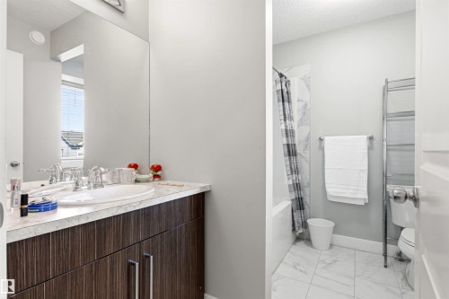 Bathroom featuring a vanity with dark wood-finish cabinetry and a light-toned countertop, a built-in tub with a tiled surround, and white tiled flooring - 9812 224 Street, Edmonton, AB - Indoor Photo Showing Bathroom