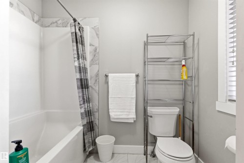 Bathroom featuring a white bathtub with a tile surround, a toilet, light gray walls, and white window blinds - 9812 224 Street, Edmonton, AB - Indoor Photo Showing Bathroom