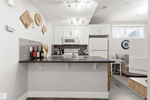 Compact kitchen featuring white cabinetry, a built-in microwave, a stainless steel sink, and a dark countertop with a breakfast bar extension - 9812 224 Street, Edmonton, AB - Indoor Photo Showing Kitchen