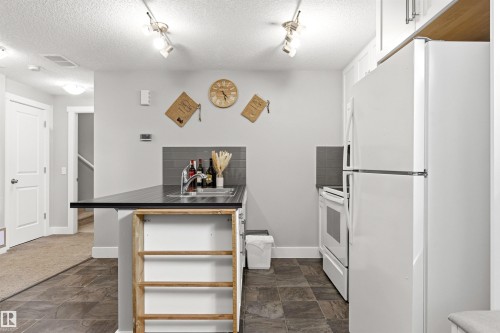 Compact kitchen featuring an integrated sink, built-in white refrigerator, and matching white electric range - 9812 224 Street, Edmonton, AB - Indoor Photo Showing Other Room
