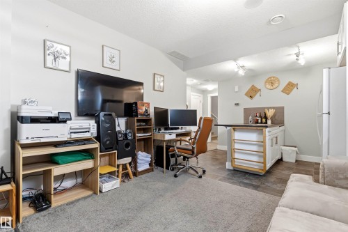 Open-concept living area with multi-zone flooring, featuring a dedicated workspace and a built-in wet bar with white cabinetry and a dark countertop - 9812 224 Street, Edmonton, AB - Indoor Photo Showing Office