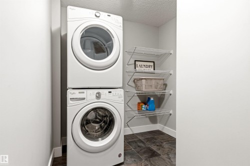 Dedicated laundry area featuring a stacked washer and dryer unit, multiple wire shelving units, and slate-finish floor tile - 9812 224 Street, Edmonton, AB - Indoor Photo Showing Laundry Room