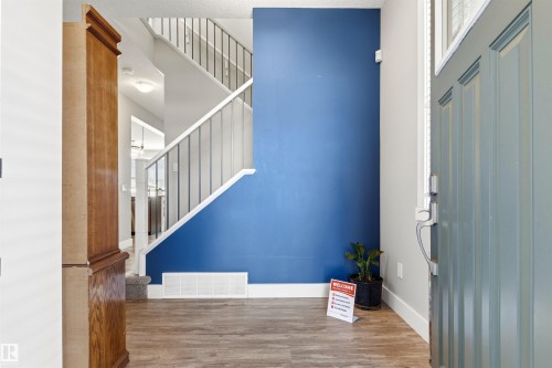 Entryway featuring wood-finish flooring, a contemporary staircase with metal railings, and a blue accent wall - 9812 224 Street, Edmonton, AB - Indoor Photo Showing Other Room