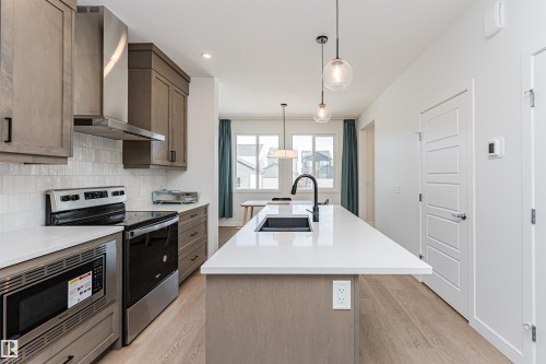 Kitchen featuring a large island with an undermount sink, quartz countertops, stainless steel appliances, and light wood-finish flooring - 3367 Erlanger Bend, Edmonton, AB - Indoor Photo Showing Kitchen With Upgraded Kitchen