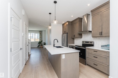 Modern kitchen featuring a central island with an integrated sink, quartz countertops, light wood-finish cabinetry, stainless steel appliances, and a tiled backsplash - 3367 Erlanger Bend, Edmonton, AB - Indoor Photo Showing Kitchen With Upgraded Kitchen