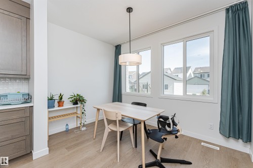 Bright dining area featuring wood-finish flooring, two large windows, a contemporary pendant light fixture, and white wall trim - 3367 Erlanger Bend, Edmonton, AB - Indoor