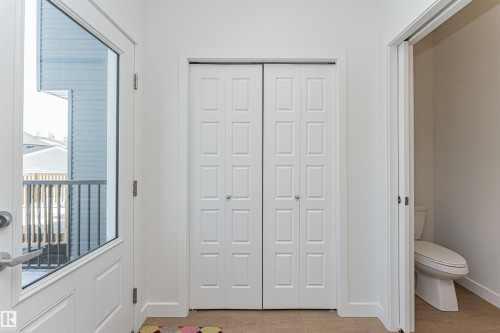 Entryway featuring a partially glass-paned door, wood-finish flooring, white paneled bifold closet doors, and a partial view of a toilet within an adjacent space - 3367 Erlanger Bend, Edmonton, AB - Indoor Photo Showing Other Room