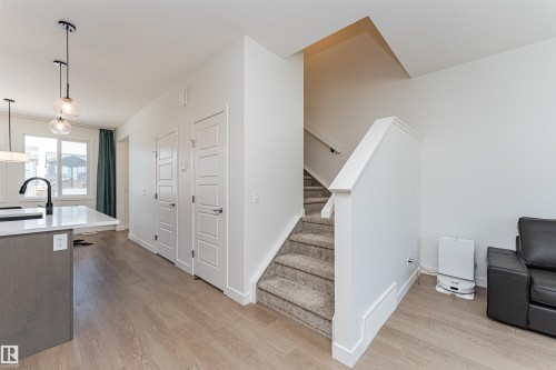 Open-concept living area featuring wood-finish flooring, a white kitchen island with a dark faucet, and a staircase with carpeted treads - 3367 Erlanger Bend, Edmonton, AB - Indoor