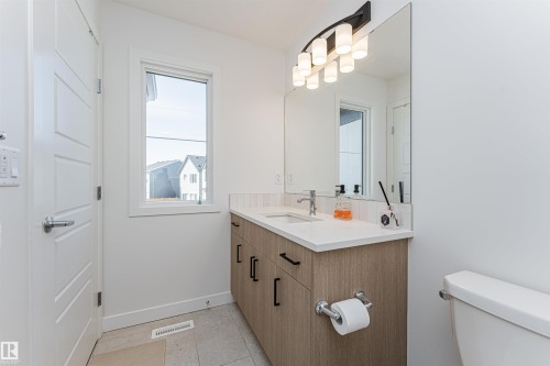 Contemporary bathroom featuring a wood-finish vanity with a white countertop and dual sinks, complemented by a large mirror and an overhead light fixture - 3367 Erlanger Bend, Edmonton, AB - Indoor Photo Showing Bathroom