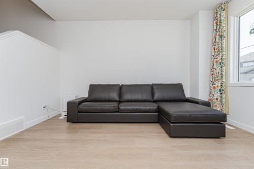 Bright interior room featuring light wood-finish flooring, white baseboards, and a large window with white trim - 3367 Erlanger Bend, Edmonton, AB - Indoor Photo Showing Living Room