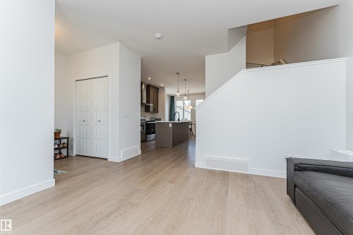 Open-concept living area featuring light wood-finish flooring, white baseboards, and a contemporary kitchen with dark cabinetry and an island - 3367 Erlanger Bend, Edmonton, AB - Indoor