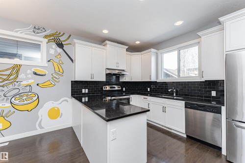 Modern kitchen featuring white cabinetry, dark wood-finish flooring, recessed lighting, and a kitchen island with a black speckled countertop - 16420 15 Avenue, Edmonton, AB - Indoor Photo Showing Kitchen With Upgraded Kitchen