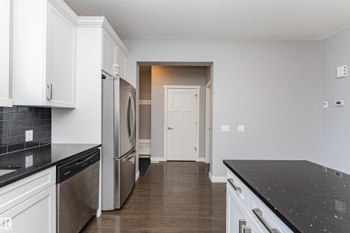 Kitchen featuring white cabinetry with crown molding, dark speckled countertops, stainless steel appliances, and a subway tile backsplash - 16420 15 Avenue, Edmonton, AB - Indoor Photo Showing Kitchen